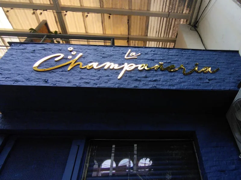 Aviso en acrílico tipo corporeo con acabado dorado instalado en fachada comercial del negocio La Champañería por Idex Publicidad en Medellín.